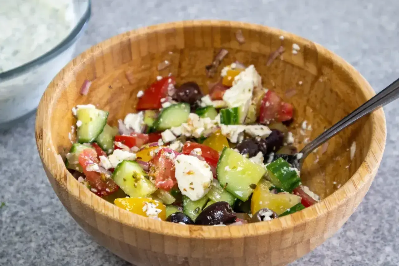 En fräsch sallad till pajen med tomat, gurka, fetaost och oliver i en träskål.