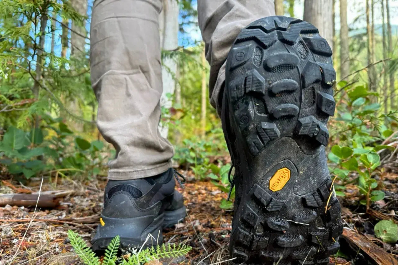 Close-up of a person's hiking boots on a forest trail, showcasing the aggressive tread pattern and the iconic yellow Vibram sole logo, highlighting the durability and grip of various Vibram sole types.