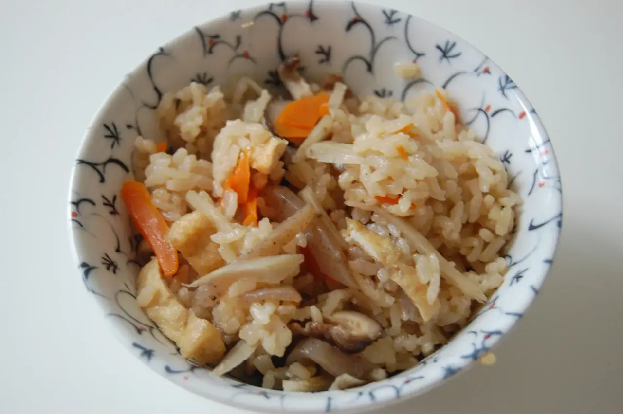 A bowl of gomoku rice, a Japanese mixed rice dish, filled with fluffy rice, tender carrots, shiitake mushrooms, and fried tofu.