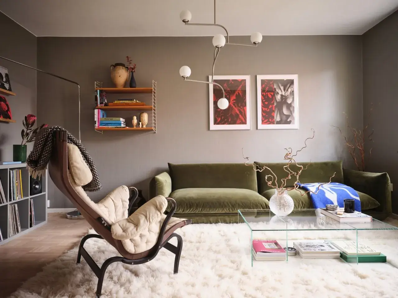 Salotto moderno con divano verde, poltrona in pelle e tessuto chiaro, tappeto bianco soffice e quadri alle pareti che creano un gioco di **colori chiari e scuri**.