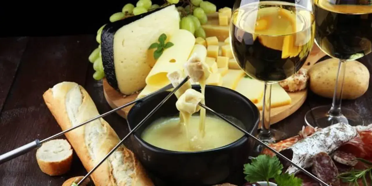 Un délicieux vin accompagne une fondue au fromage, avec du pain, des pommes de terre et de la charcuterie.