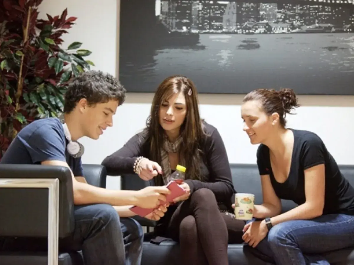 Jóvenes planeando su intercambio en Londres, sentados en un sofá, con una planta y un cuadro de la ciudad de fondo.