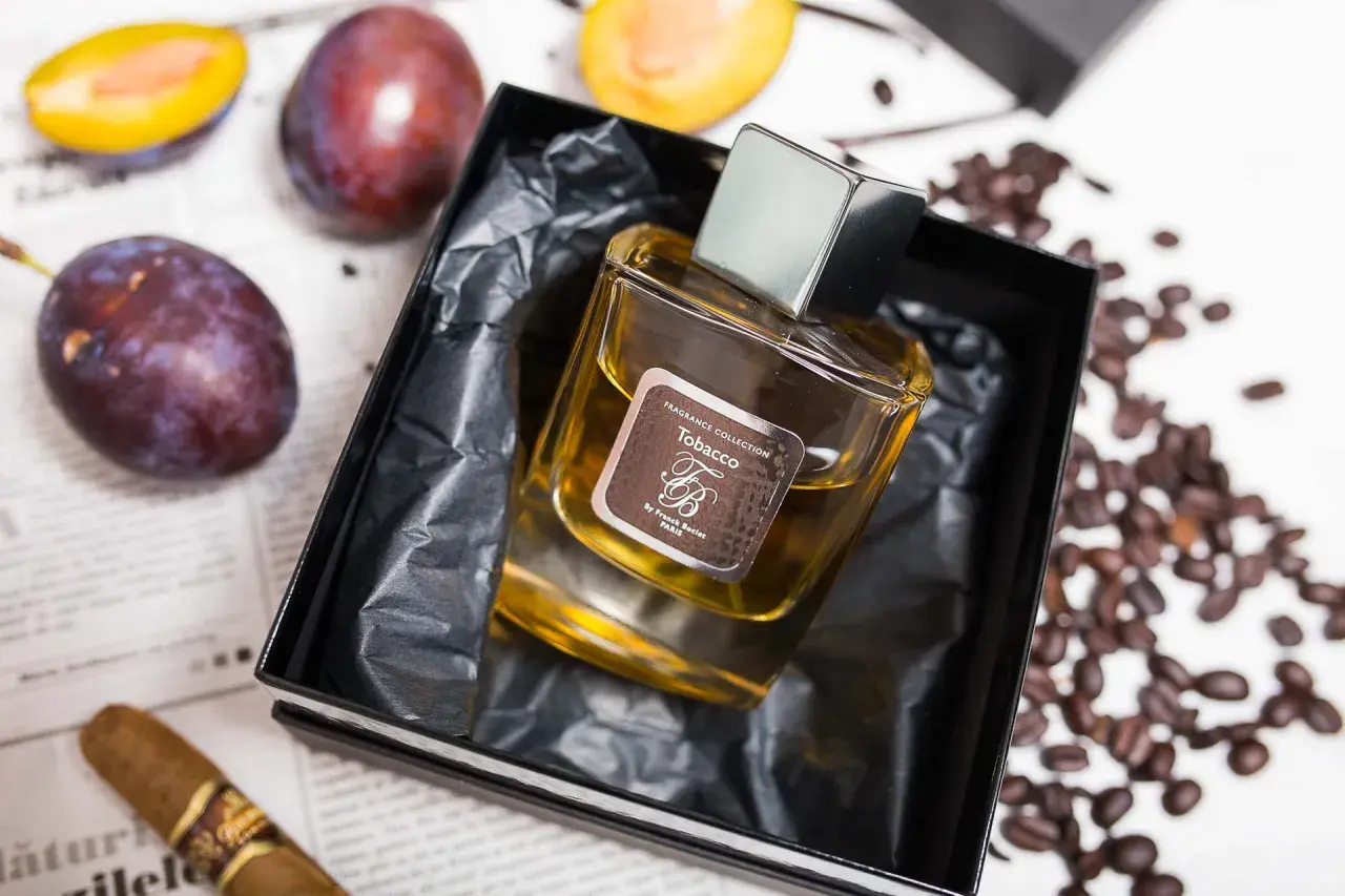 Perfumy "Tobacco" by Franck Boclet w eleganckim flakonie, otoczone śliwkami, kawą i cygarem.