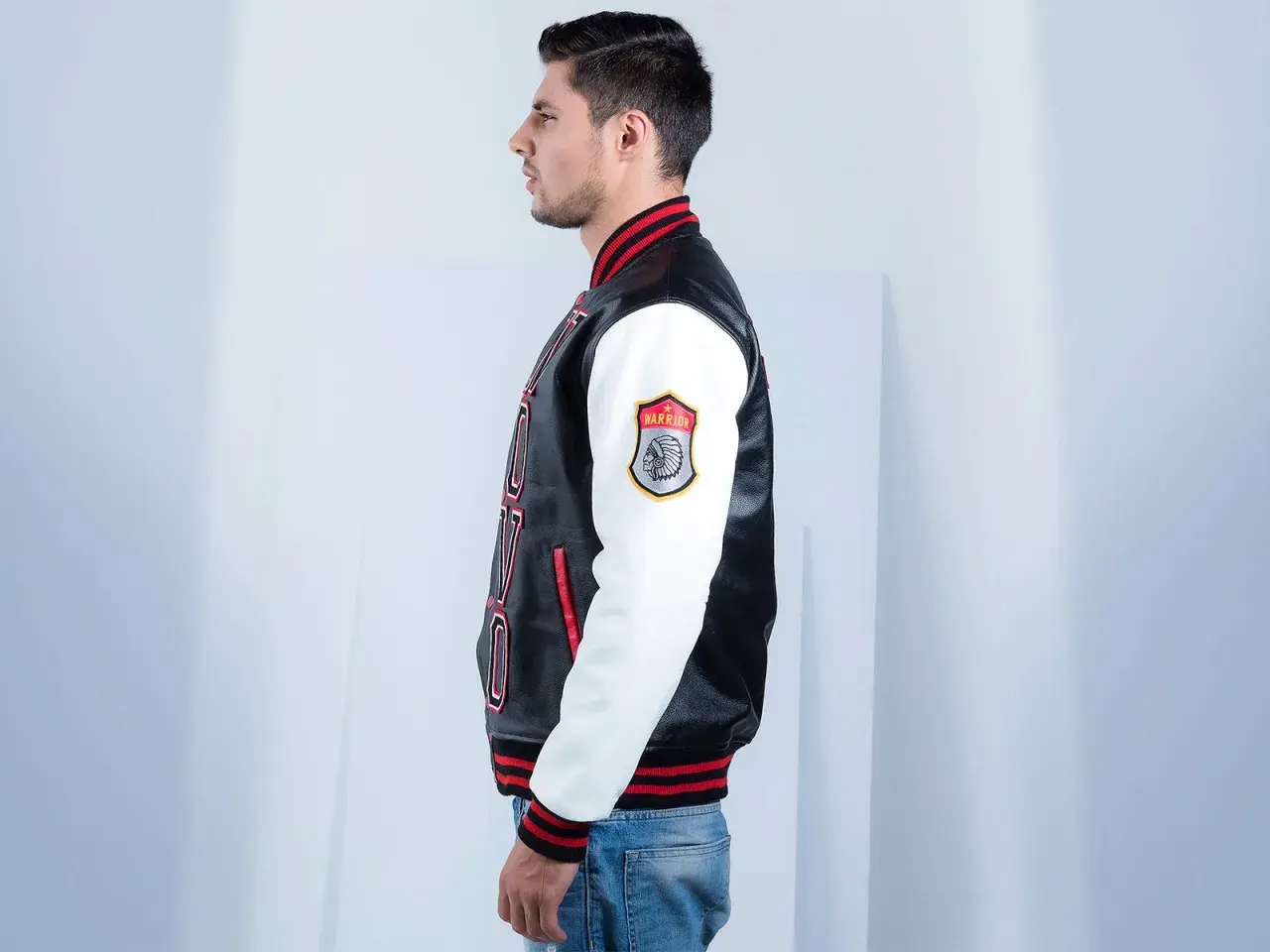 Man in profile wearing a black and white letterman jacket with red trim and a "Warrior" patch.