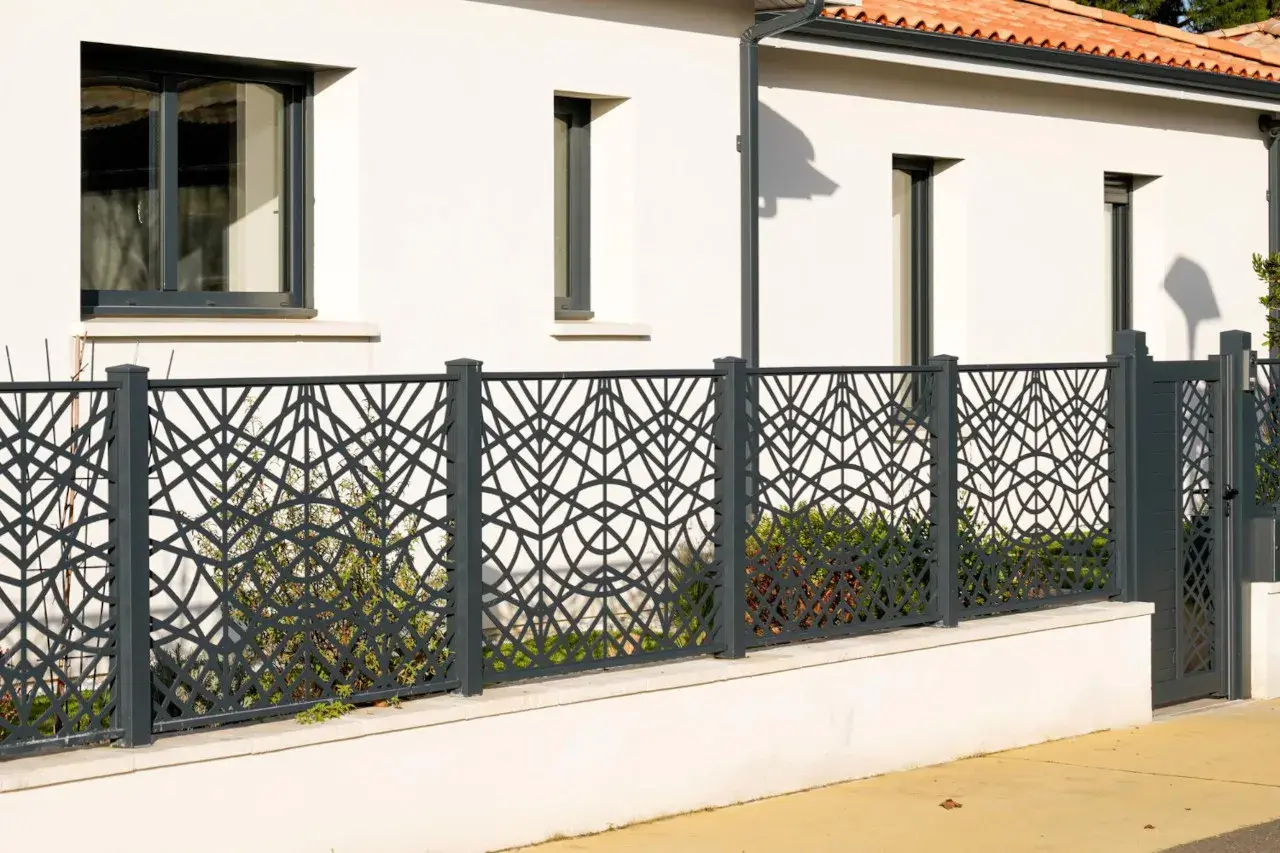Nowoczesne, ciekawe ogrodzenia posesji z metalowymi panelami o geometrycznym wzorze liści. Elegancko oddzielają dom od ulicy.