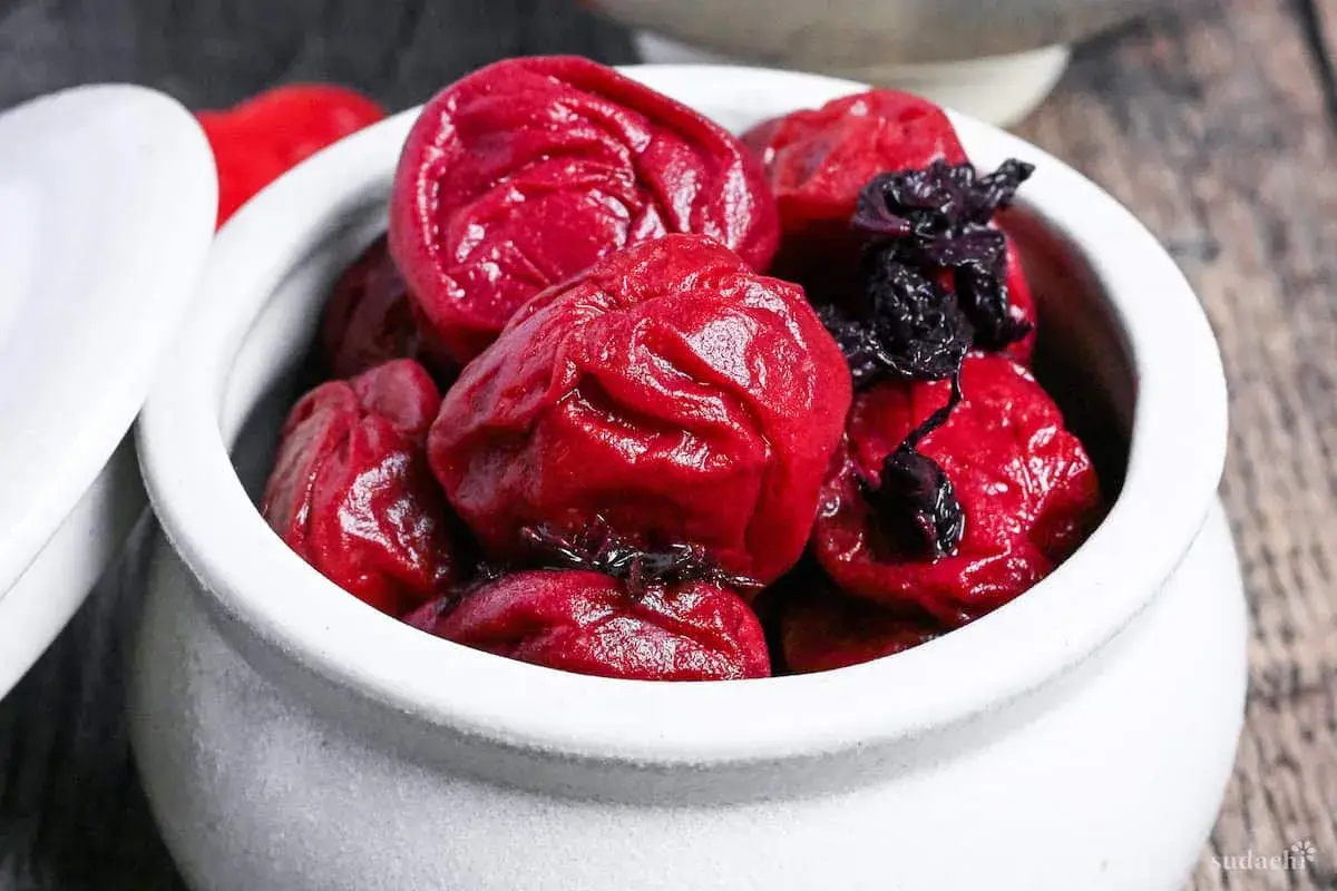 A white ceramic bowl filled with glistening, deep red umeboshi plums, ready for a delicious umeboshi recipe.