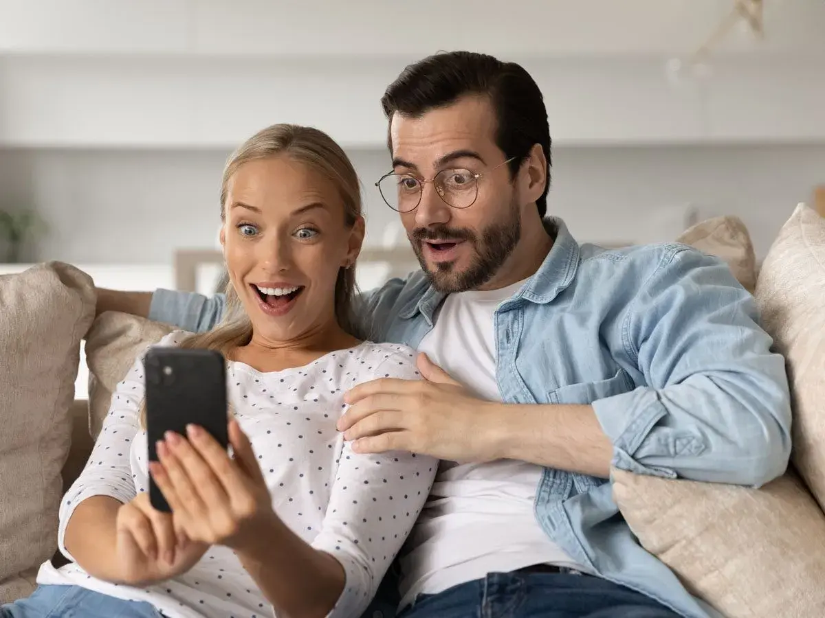 Para ogląda na telefonie, śmiejąc się z głupich pytań. Ich miny wyrażają zdziwienie i rozbawienie.