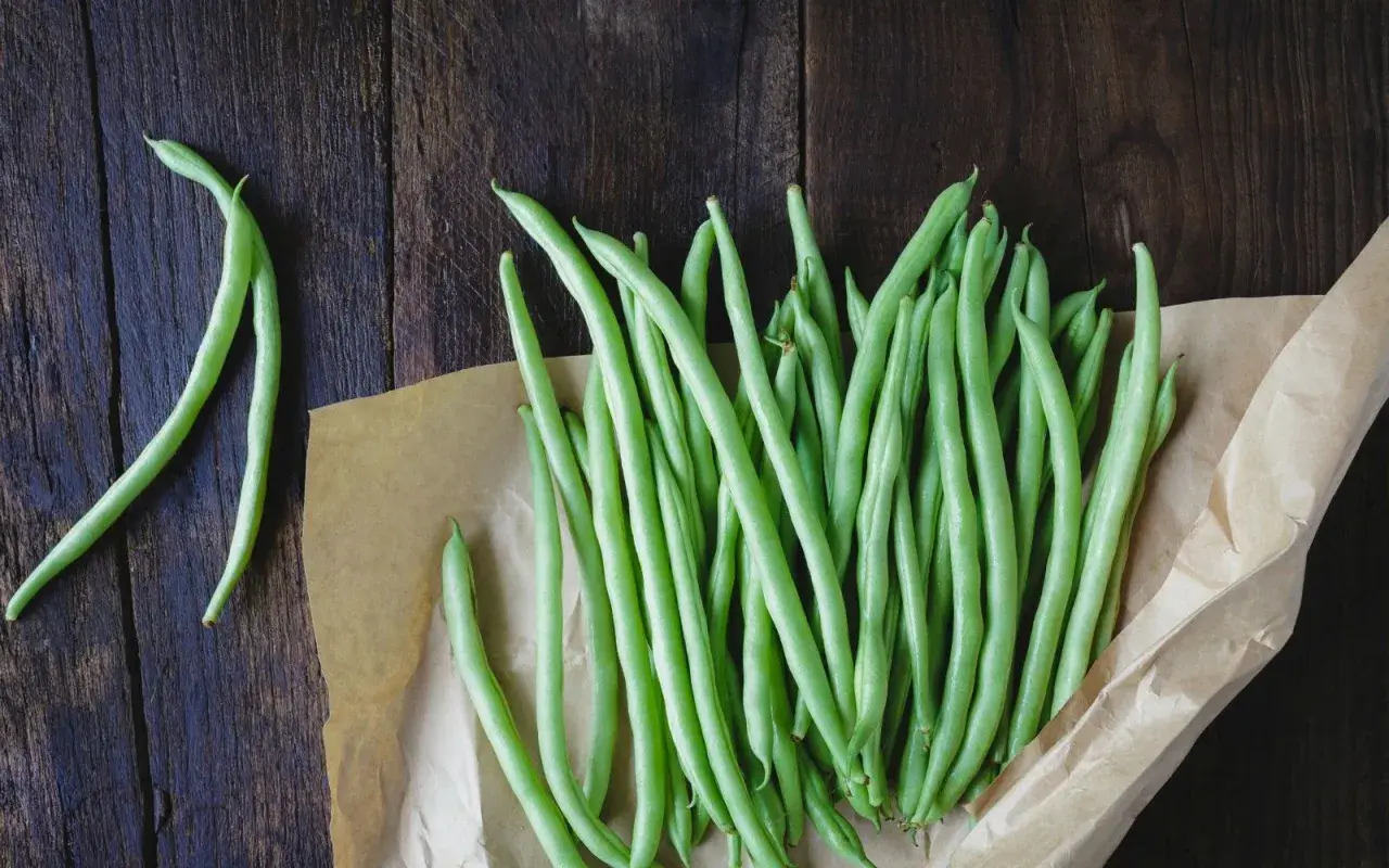 Fagiolini freschi pronti per essere bolliti in acqua fredda o calda, disposti su carta da forno su un tavolo di legno scuro.