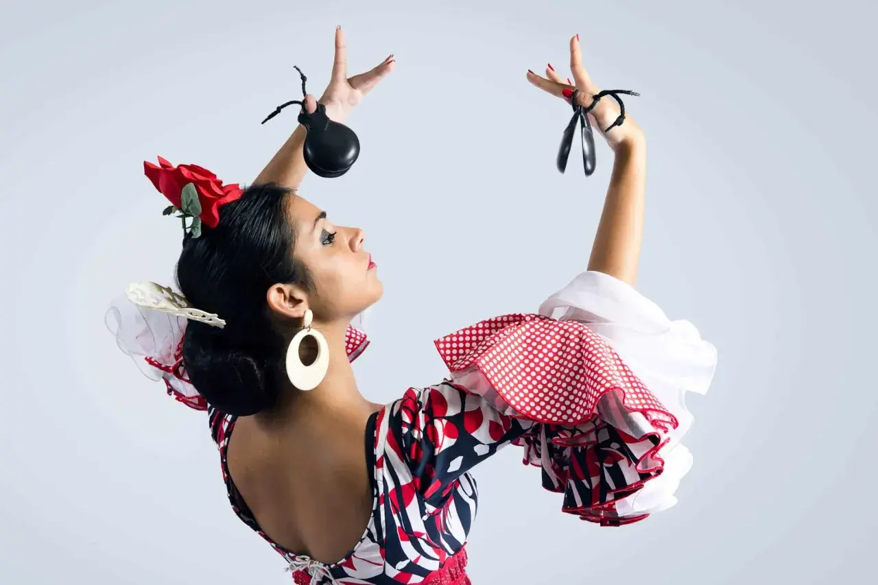 Bailarina flamenca con castañuelas y peinados sevillana, luciendo un vestido de lunares y volantes.