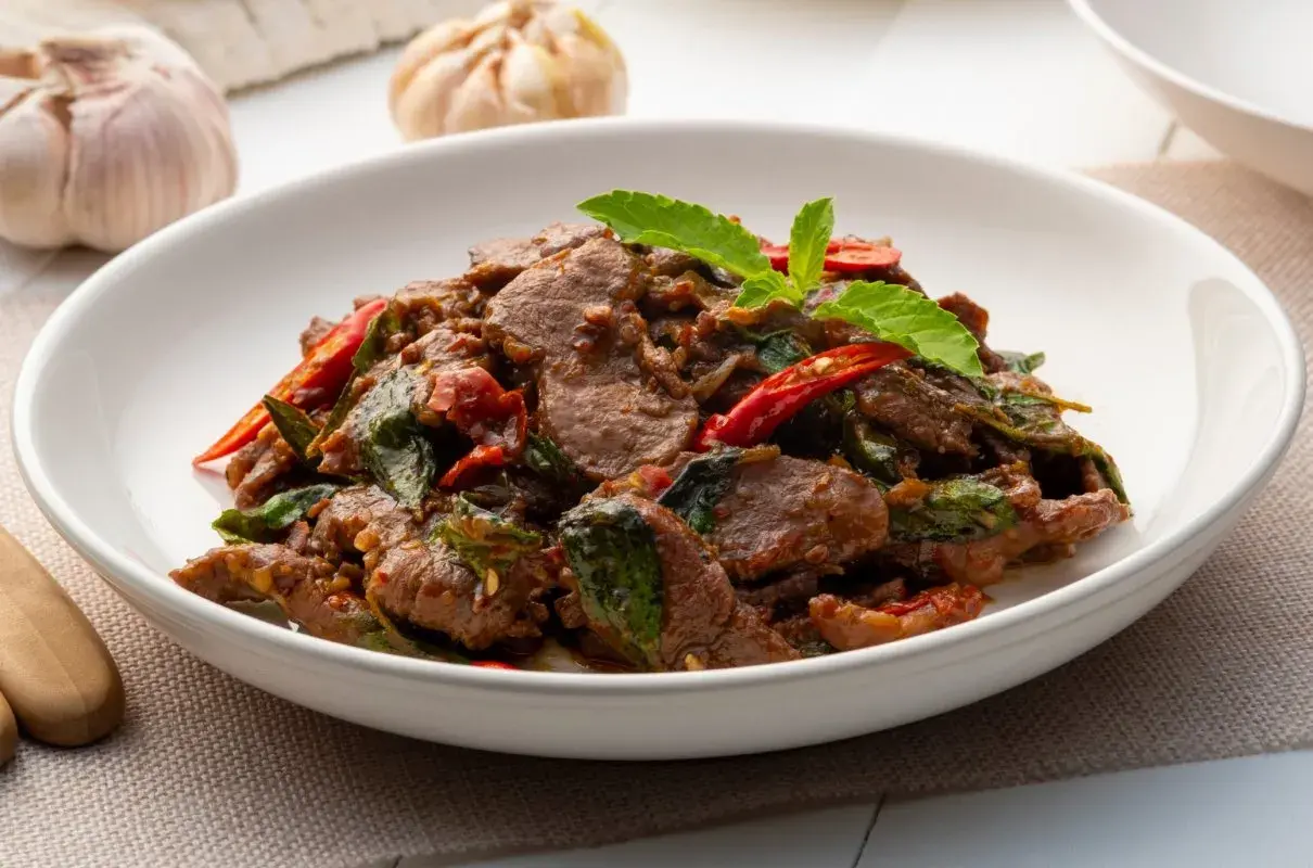 Aksamitne kawałki wołowiny po tajsku z bazylią i papryczką chili, podane w białej misce.