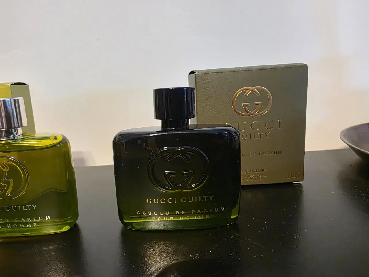 Dwie butelki perfum Gucci Guilty na ciemnym tle, jedna z nich z pudełkiem.