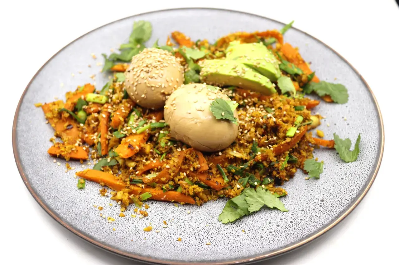 Assiette de riz aux légumes et deux oeufs marinés japonais, parsemée de graines de sésame et de coriandre fraîche.