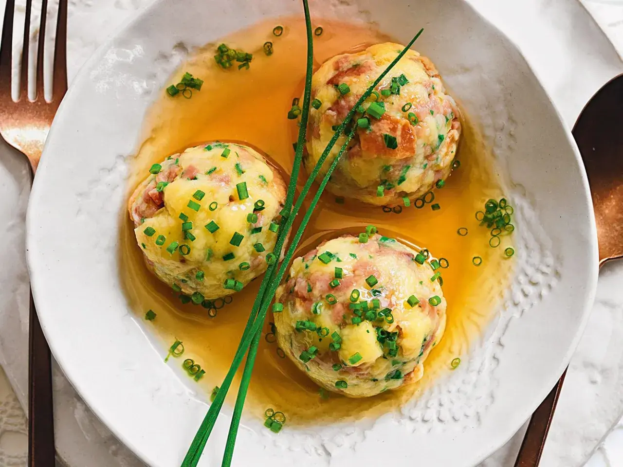 Tre canederli in brodo, guarniti con erba cipollina. Una deliziosa ricetta per un piatto tradizionale.