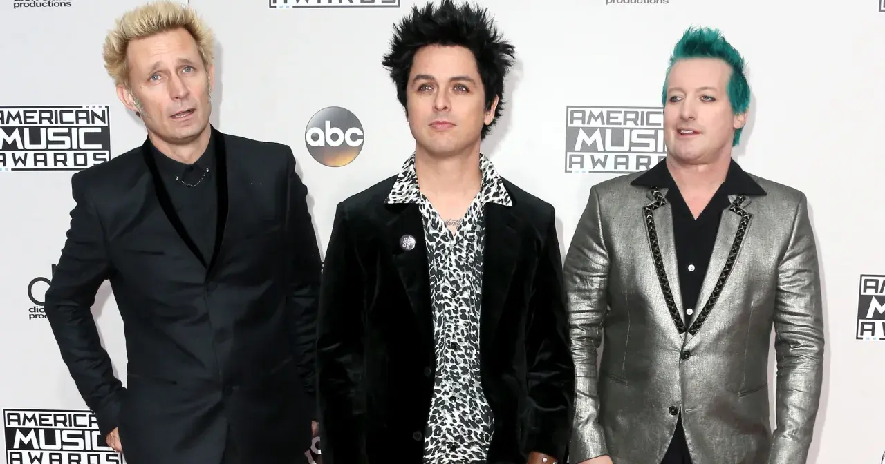 Trzech członków Green Day: Billie Joe Armstrong, Mike Dirnt i Tré Cool, pozują na czerwonym dywanie.