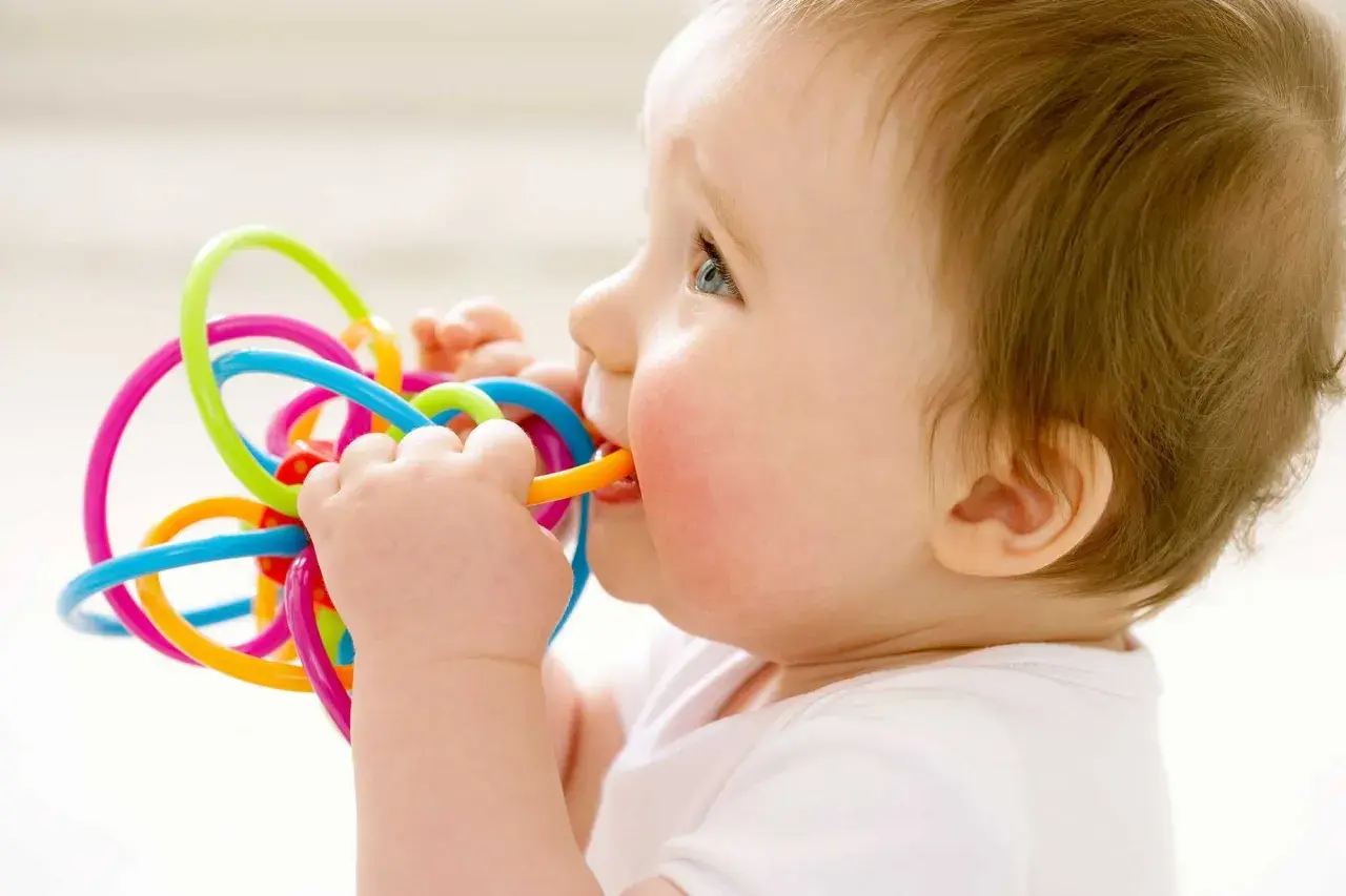 Bambino di 1 anno con dolore ai denti, che morde un giocattolo colorato per alleviare il fastidio.