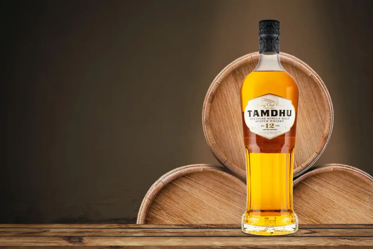 Butelka whisky single malt Tamdhu 12 lat, stojąca na drewnianych beczkach.