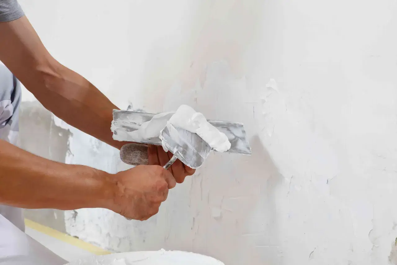 Man aplicando revoco en una pared con una llana. El revoco es un material de construcción para alisar y proteger superficies.