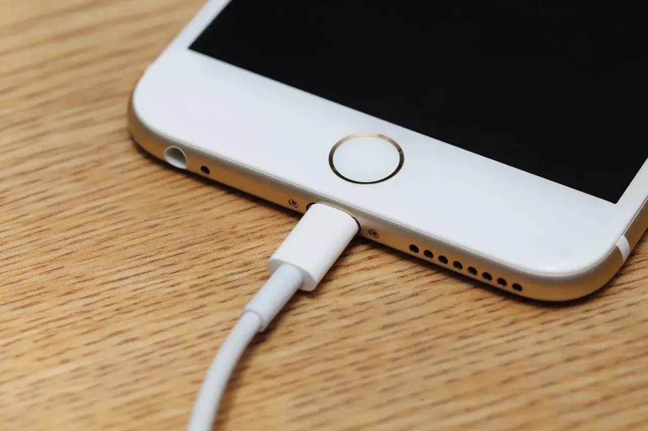Zablokowany iPhone podłączony do komputera. Ekran jest czarny, a kabel ładujący wpięty do portu.