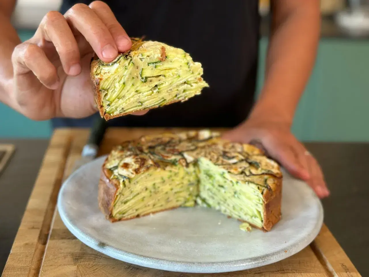 Une main tient une part d'un gâteau aux courgettes, révélant ses fines couches. Ce délice est presque invisible aux courgettes, tant elles sont bien intégrées.
