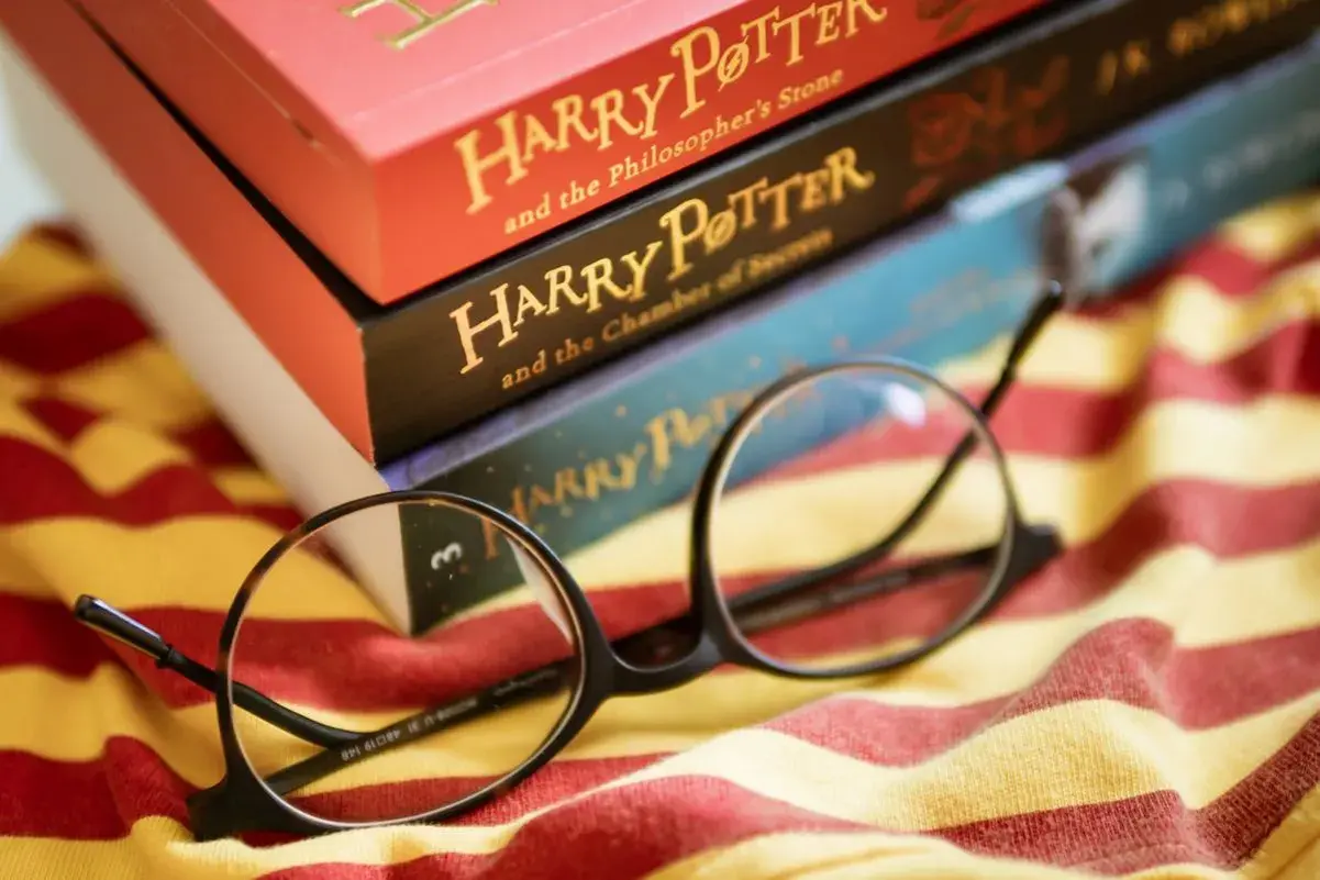 Okulary Harry'ego Pottera leżą na tle książek z serii i szalika Gryffindoru. To idealny cytat z Harrego Pottera dla każdego fana.