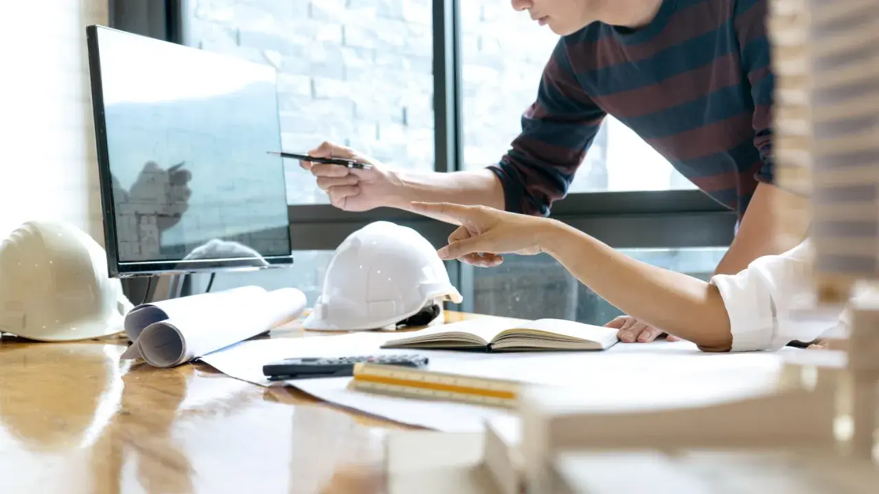 Deux architectes discutent d'un plan sur un écran, utilisant un système de gestion de contenu d'entreprise pour organiser leurs documents.