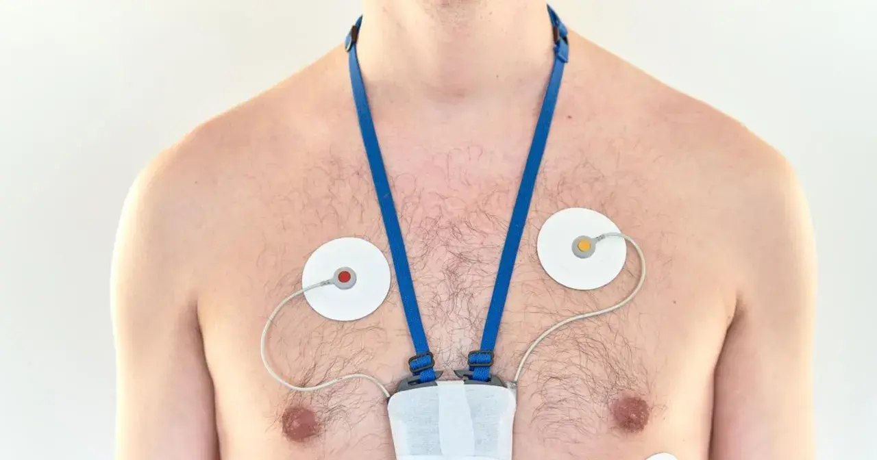 Mężczyzna z przyklejonymi elektrodami i urządzeniem na klatce piersiowej, monitorującym jego serce. To holter ciśnieniowy.