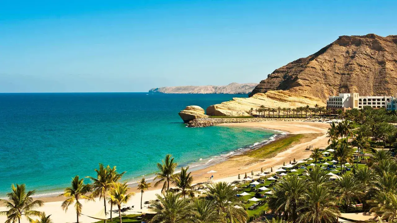 Traumhafte Bucht mit Palmen, Sandstrand und Felsen. Ein Hotel am Hang. Perfekt für Oman Reisetipps.