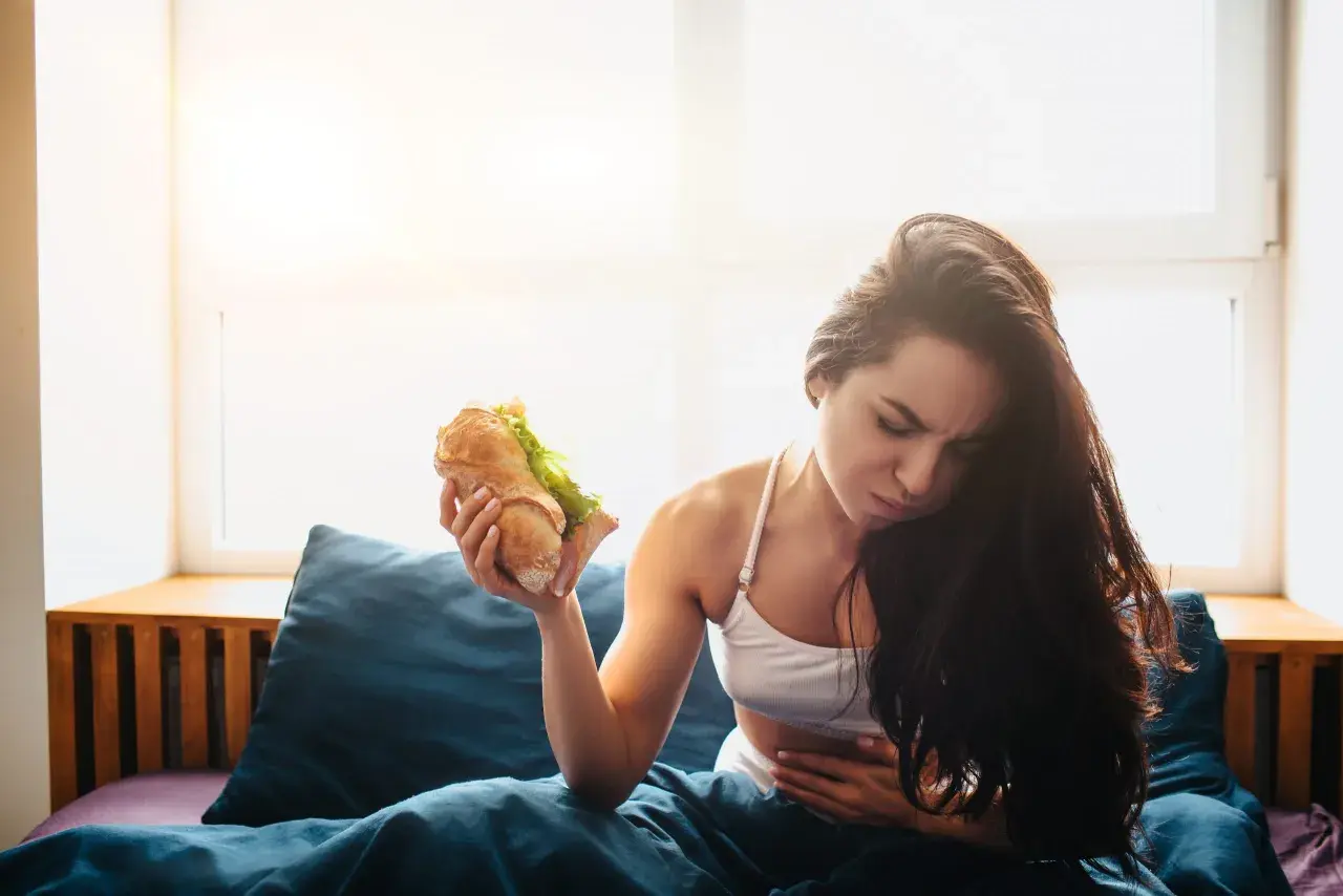 Donna con mal di stomaco tiene un panino, pensando cosa mangiare dopo aver vomitato.