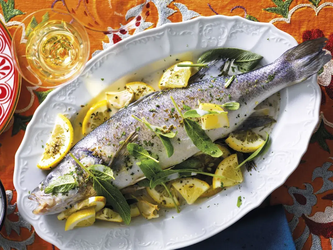 Un succulento branzino in padella, guarnito con spicchi di limone e foglie di salvia, pronto per essere gustato.