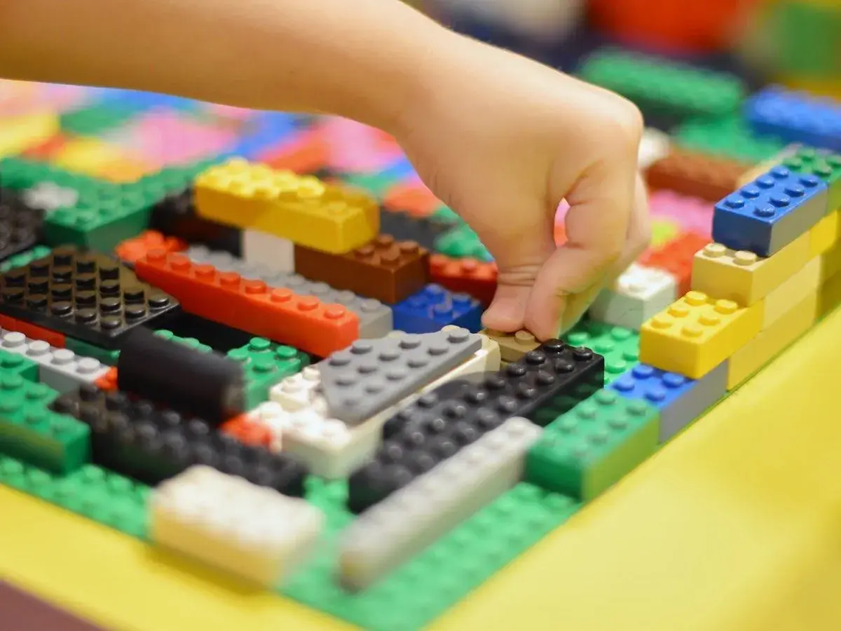 Kind baut mit bunten LEGO-Steinen. Viele LEGO-Ideen zum Nachbauen sind hier zu sehen, von einer Hand, die einen Stein platziert.