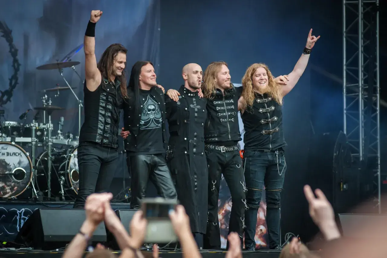 Zespół Beast in Black na koncercie, pięciu muzyków w czarnych strojach pozuje na scenie.