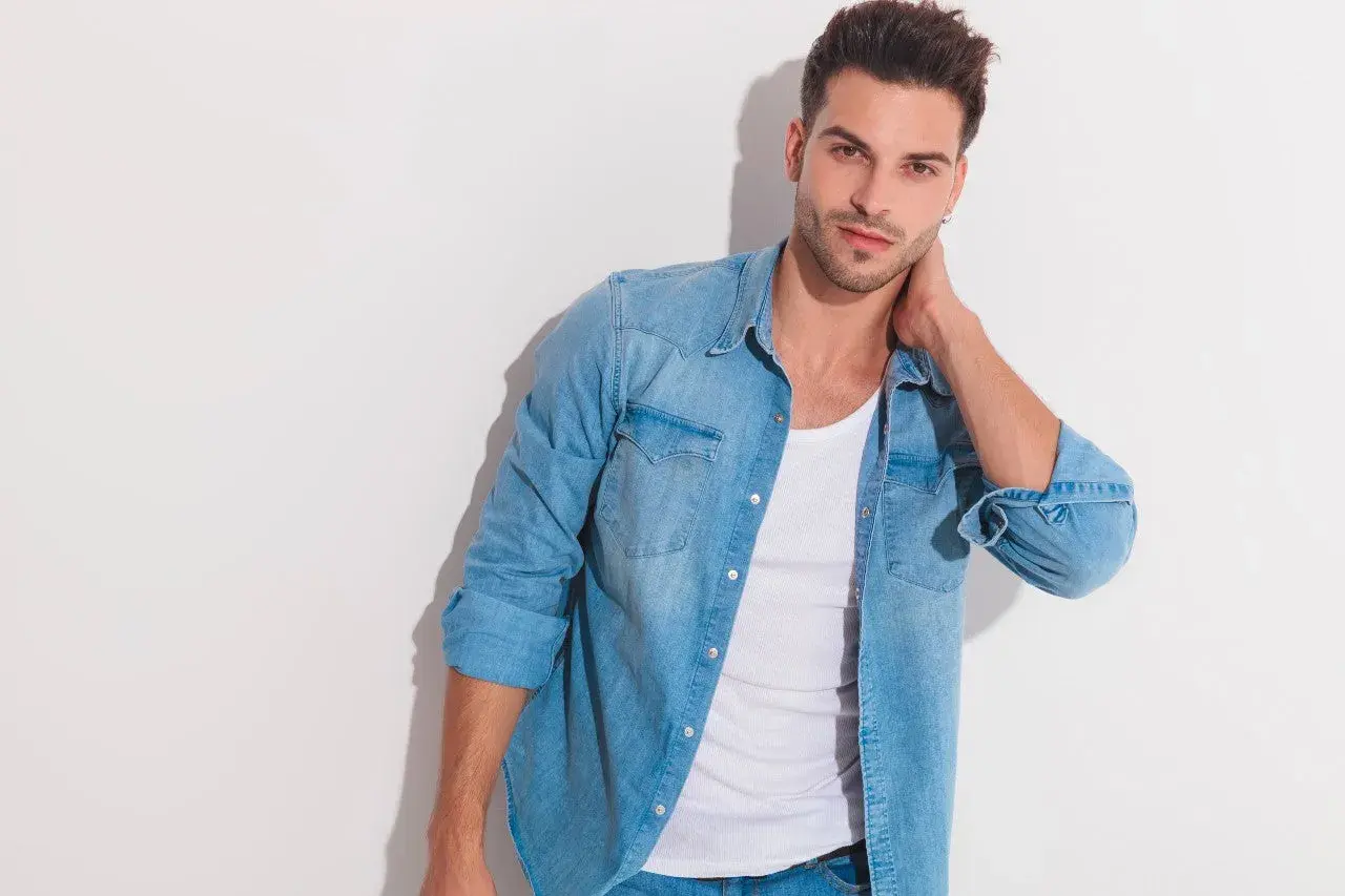 Junger Mann mit lässigem Look: blaues Jeanshemd über einem weißen Unterhemd unter T-Shirt.