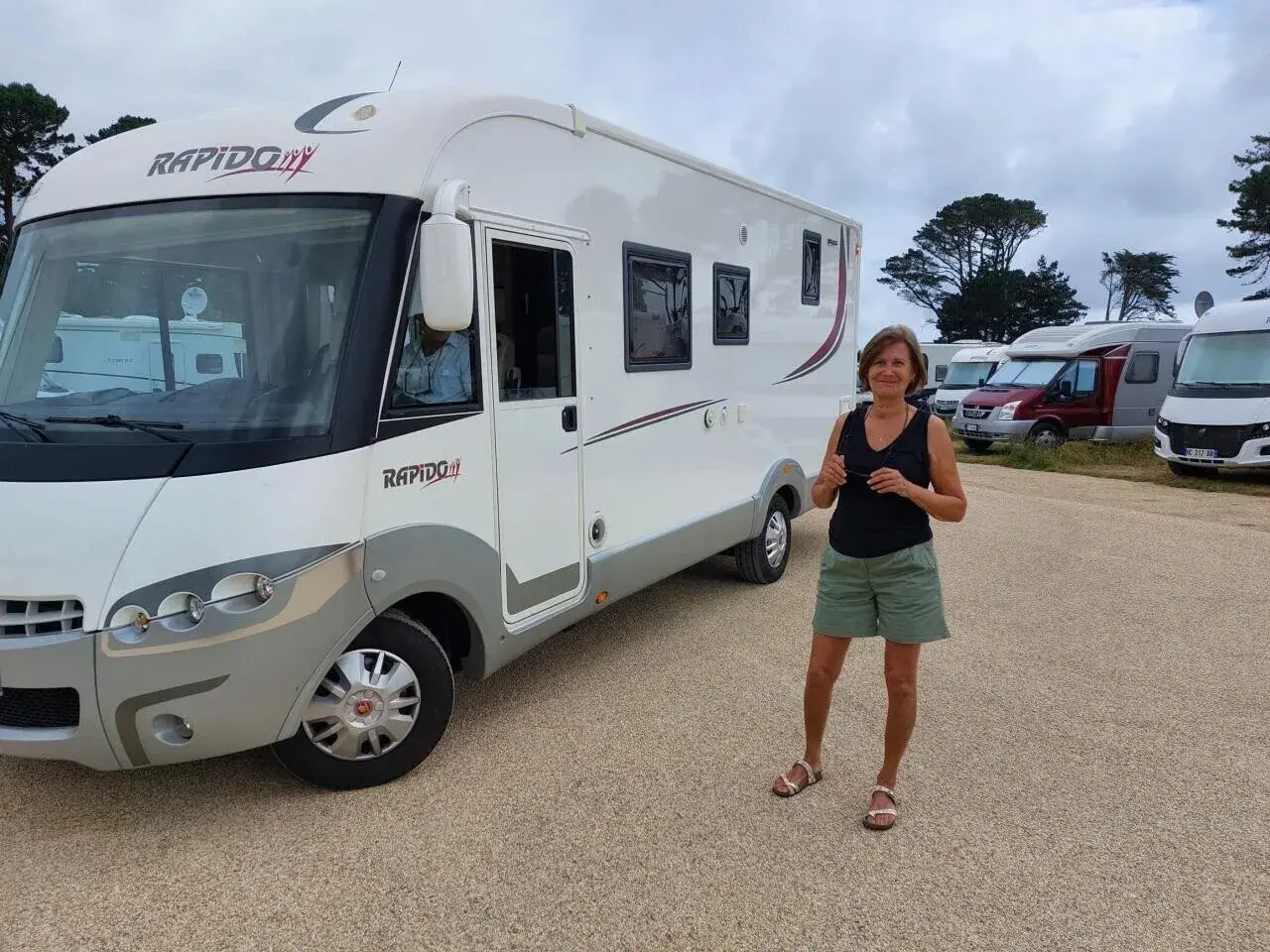 Une femme pose devant son camping-car Rapido, sur une aire de camping-car près de la Côte de Granit Rose.