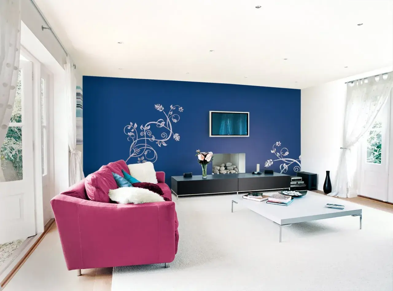 Un salone moderno con divano fucsia e parete blu con decorazioni floreali. Idee per come pitturare un salone con stile.