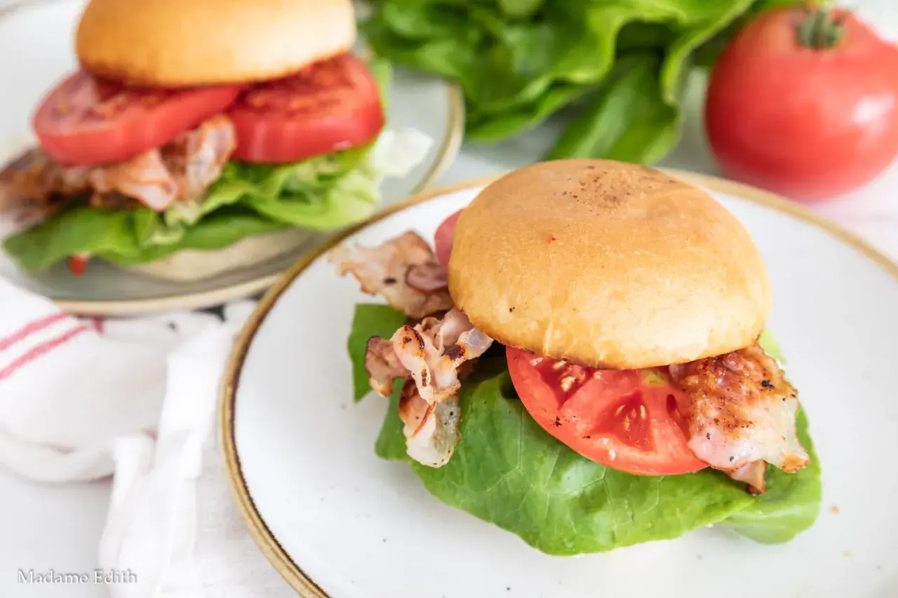 Dwa pyszne BLT na talerzach, z chrupiącym bekonem, soczystymi pomidorami i świeżą sałatą. Idealne na szybki lunch.