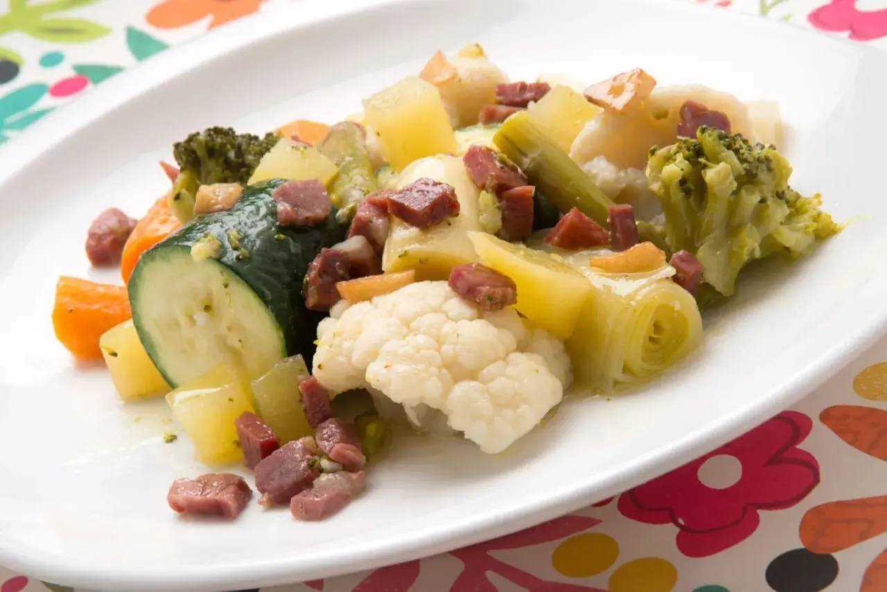 Un colorido panache de verduras con brócoli, coliflor, calabacín, zanahoria y patatas, salpicado de trocitos de jamón.