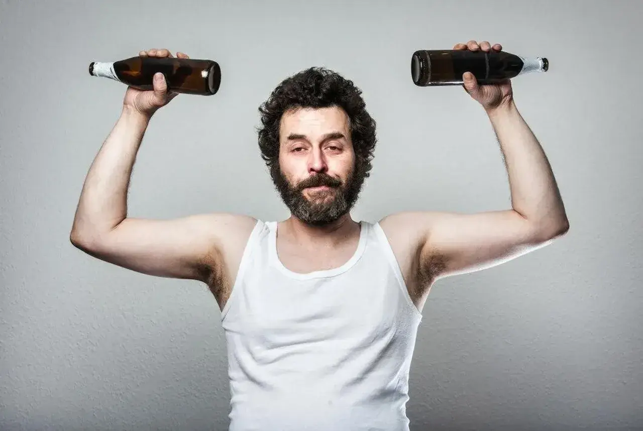 Mężczyzna w białej podkoszulce podnosi dwie butelki, symbolizując wpływ testosteronu a alkoholu na siłę i samopoczucie.