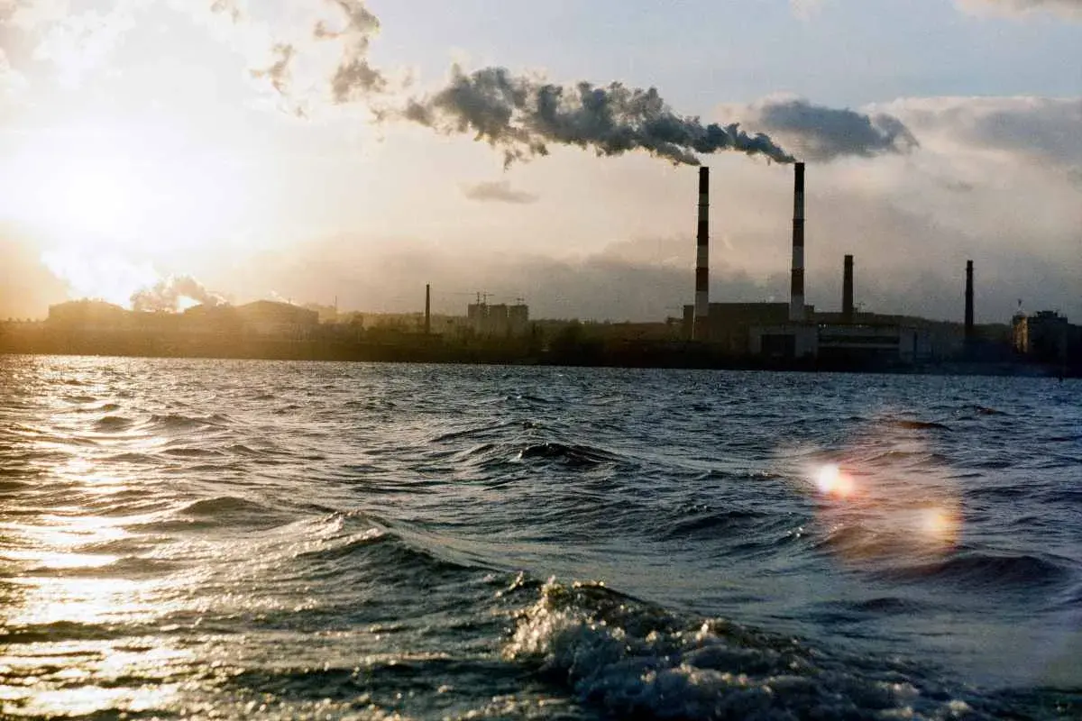 Chimeneas industriales emiten humo sobre un río, un ejemplo de cómo se mide la calidad del aire.