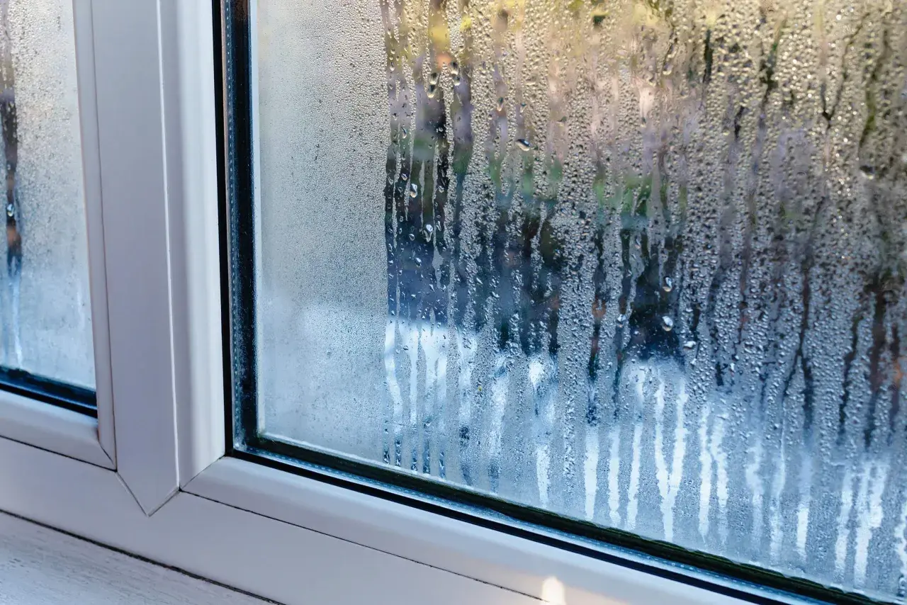 Gouttes d'eau ruisselant sur une fenêtre, signe de condensation. La lumière du jour filtre à travers les gouttelettes.