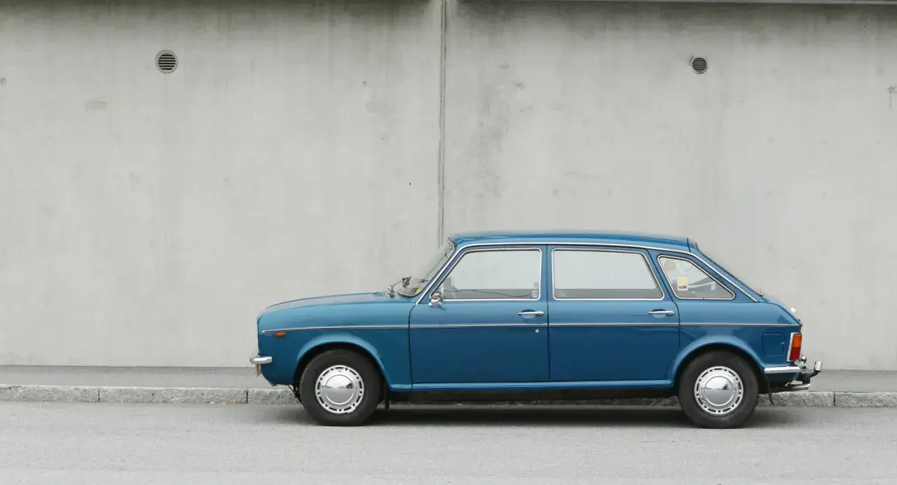 Blå Austin Maxi parkerad vid en betongvägg. En klassisk bil som väcker minnen.