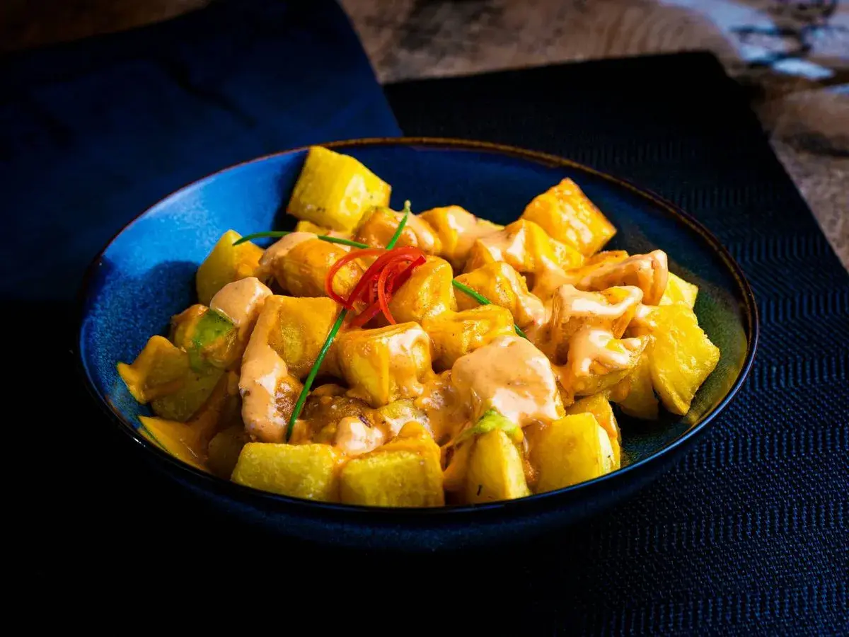 Patatas bravas receta: trozos dorados de patata cubiertos con una cremosa salsa rosada y decorados con pimiento rojo y cebolleta.