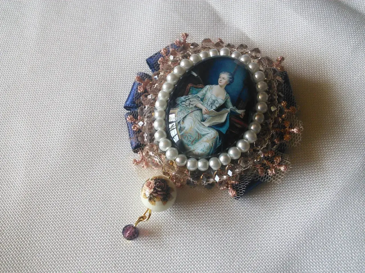 Broche con camafeos, perlas y detalles florales. Una dama elegante lee un libro en un retrato ovalado, rodeada de encaje y cristales.