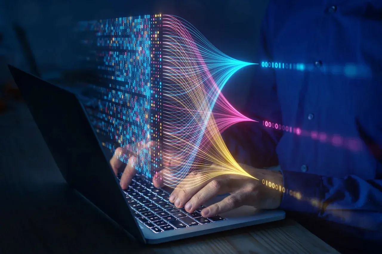 Ręce na klawiaturze laptopa, wizualizacja danych w postaci kolorowych linii i kodu binarnego. Przyszłość elektrotechniki w cyfrowym świecie.