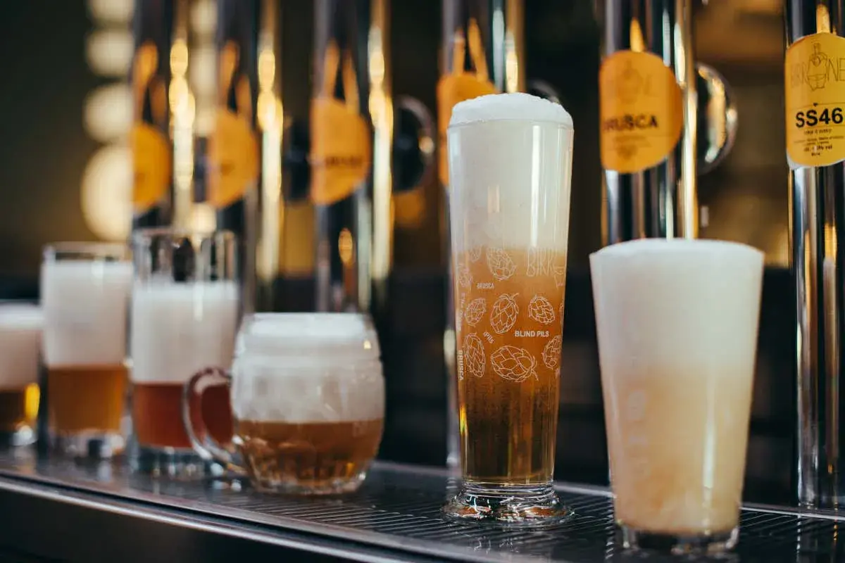 Bicchieri di birra con schiuma abbondante, tra cui una rye ipa decorata con luppoli.