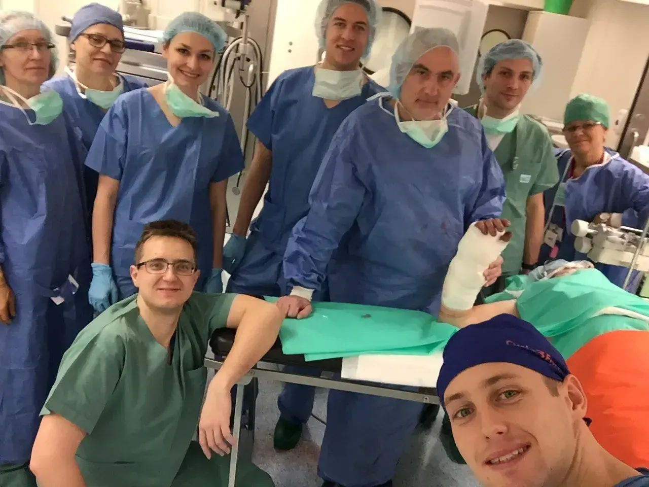 Zespół chirurgów w strojach operacyjnych pozuje do zdjęcia w sali operacyjnej, jeden z nich trzyma nogę w gipsie.