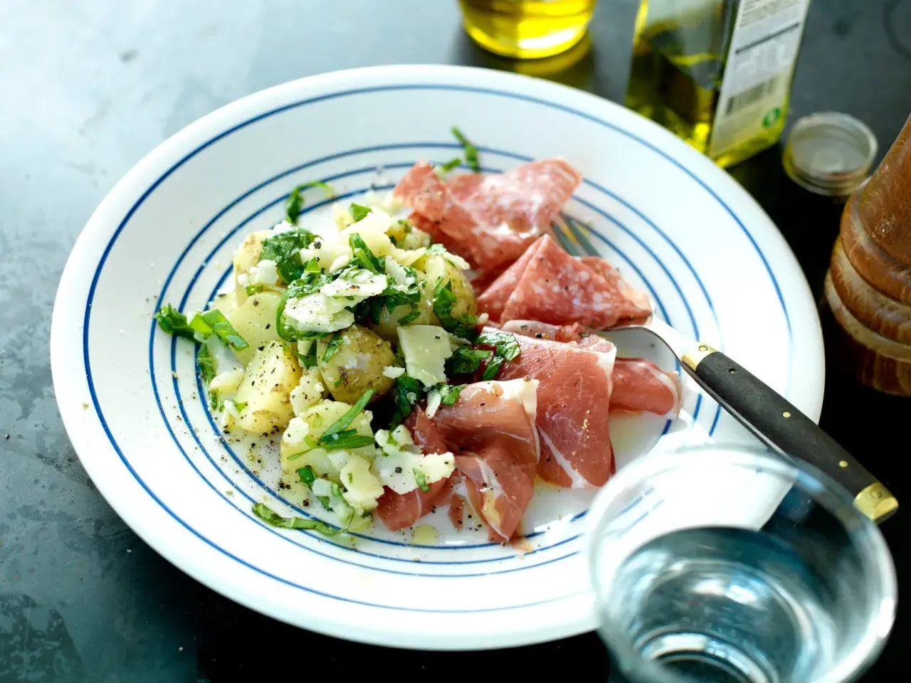 En tallrik med potatissallad med parmesan, serverad med salami och prosciutto. En utsökt måltid!