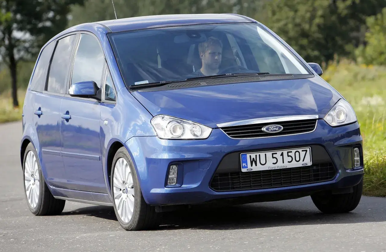 Niebieski Ford C-Max 1.6 benzyna z mężczyzną za kierownicą jedzie po drodze wśród zieleni.
