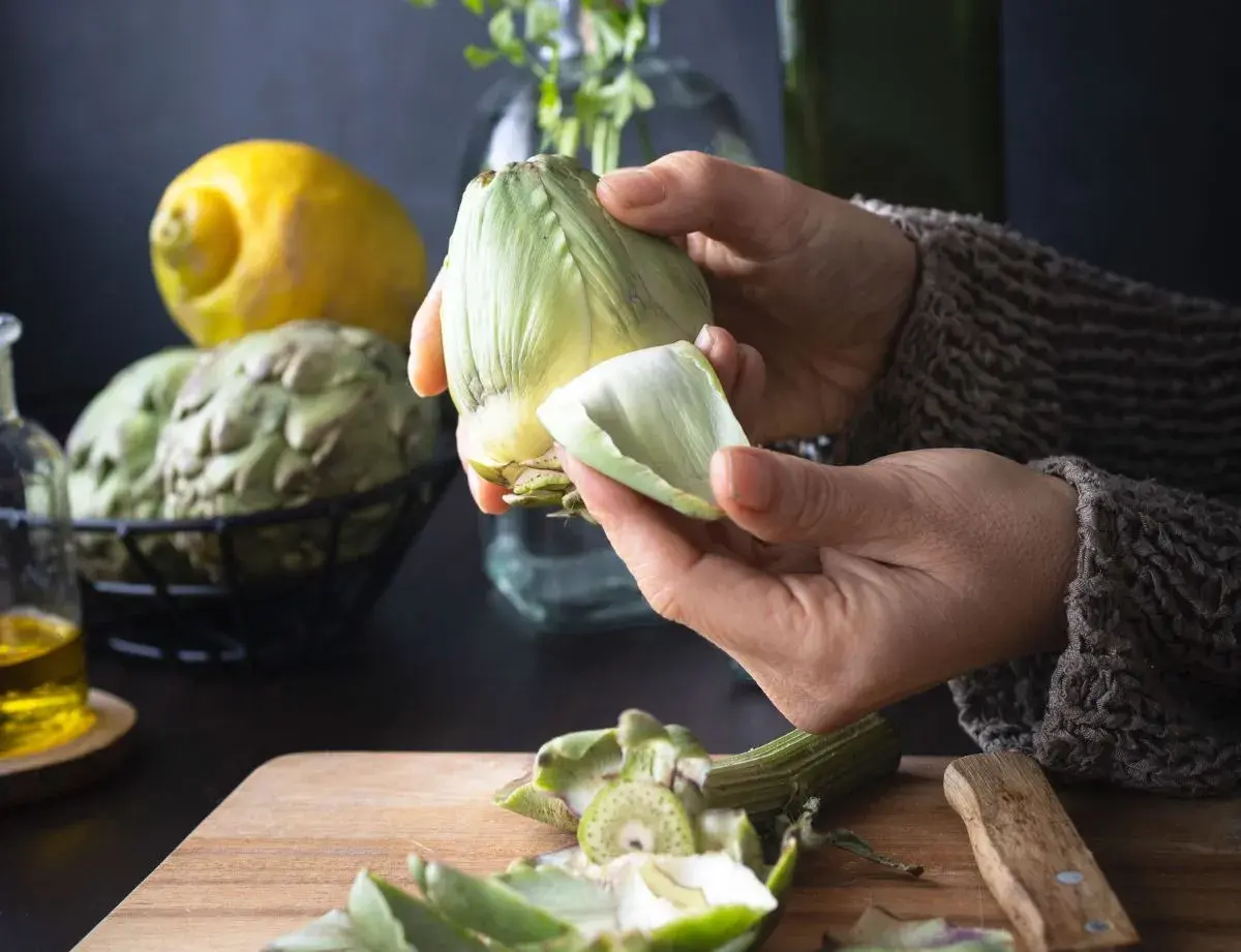 Manos preparan alcachofas para deliciosas recetas. Limón y aceite de oliva a la vista.