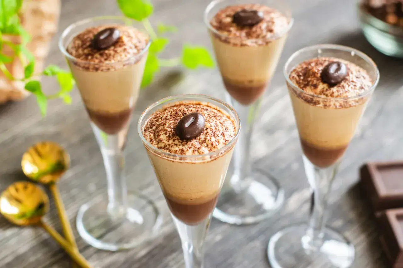 Quattro bicchieri di deliziosa mousse al caffè, spolverata di cacao e guarnita con un chicco di caffè.