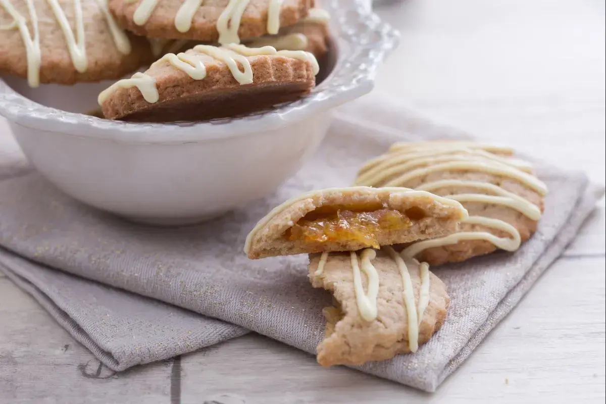 Galletas de espelta rellenas de mermelada, cubiertas con glaseado blanco.